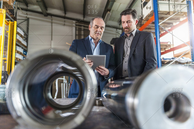 Two engineers with digital tablet in front of hydraulic cylinder