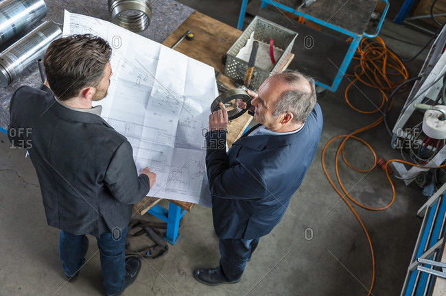 Two engineers with construction plan talking, hydraulic cylinder