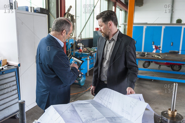 Two engineers with digital tablet, construction plan in front of hydraulic cylinder