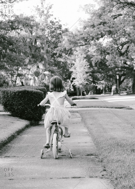 Girl riding a bike with training wheels on the sidewalk