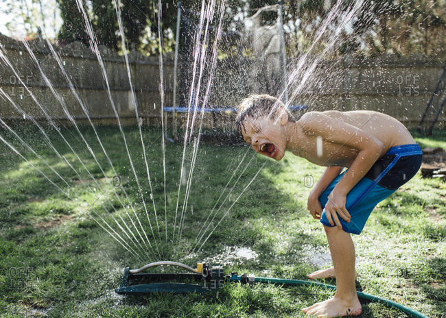 Young boy drinking from a sprinkler in his backyard