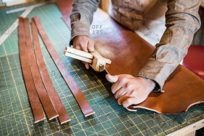 Hands of leather craftsman using wooden clamp on workshop bench