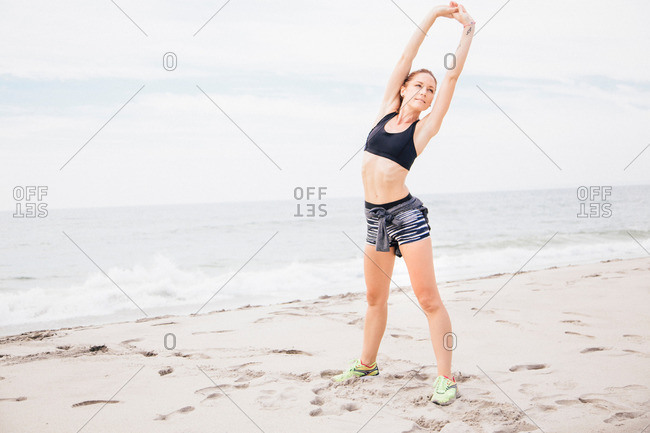 Portrait of mid adult woman standing on beach, hands over head, stretching