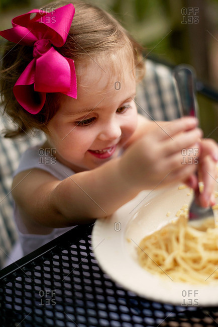 High angle view of girl with pink hair bow sitting at garden eating spaghetti