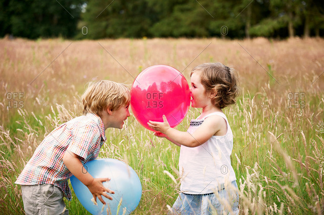 Brother and sister in tall grass face to face playing with balloon