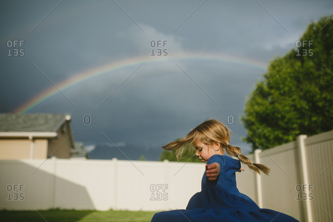 Girl spinning in circles in her backyard under a rainbow