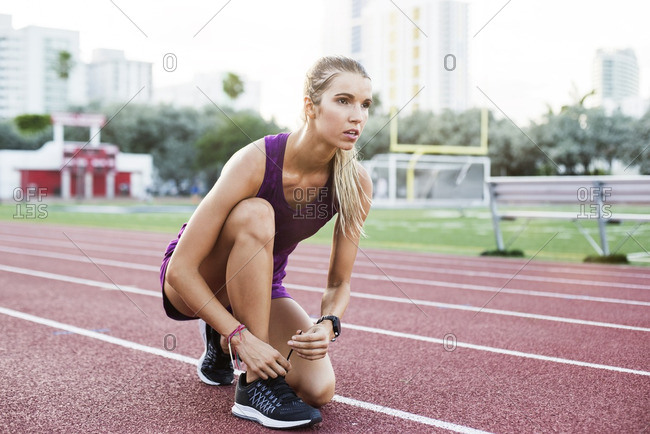 Confident female athlete tying shoelace on race tracks