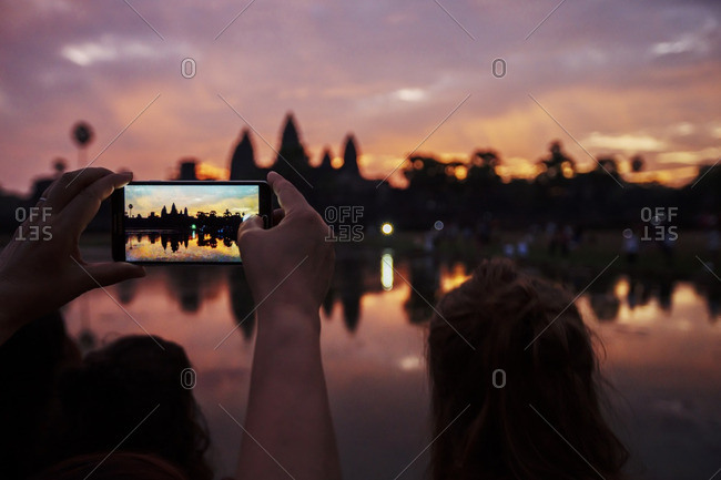 Cropped image of tourist photographing silhouette Angkor Wat temple during sunset
