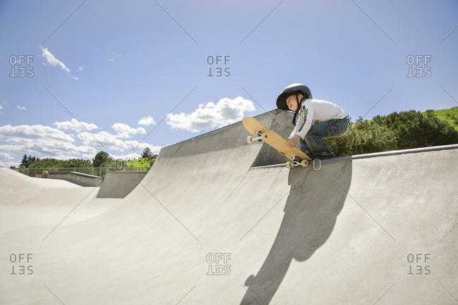 Low angle view of boy holding skateboard on ramp against blue sky