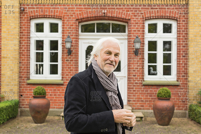 Portrait of senior man wearing jacket and scarf outside house
