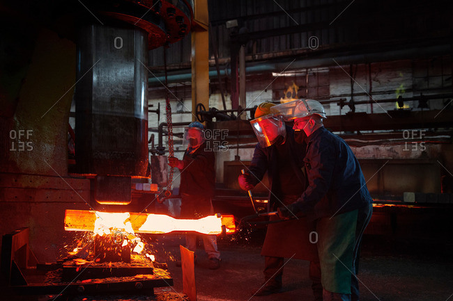 Forge workers pre form red hot steel billet into flight bar (mining component) on hammer