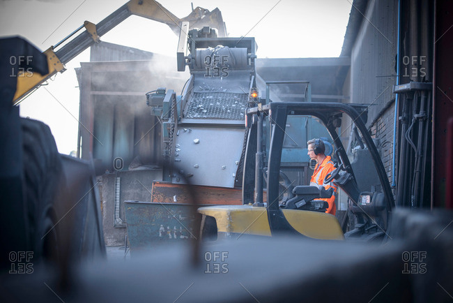 Worker watching machinery crush titanium metal