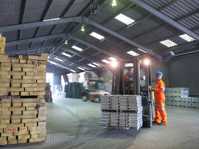 Worker checking delivery of metal alloy with fork lift driver in port store