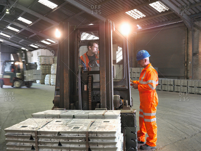 Worker and fork lift driver checking delivery of metal alloy