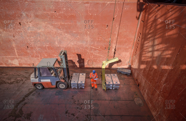 High angle view of worker checking metal alloy ingots in ship's hold