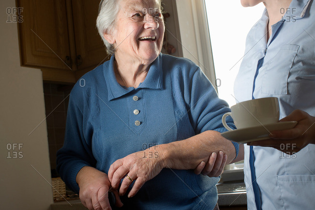 Personal care assistant carrying cup of tea for senior woman