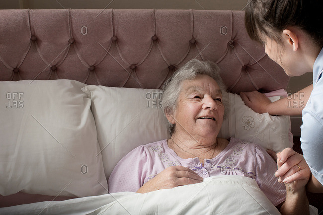 Personal care assistant chatting to senior woman in bed
