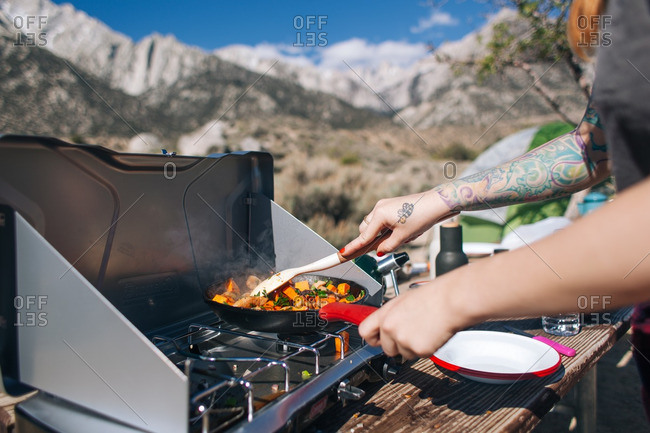 Tattooed woman cooking outdoors on a camp stove