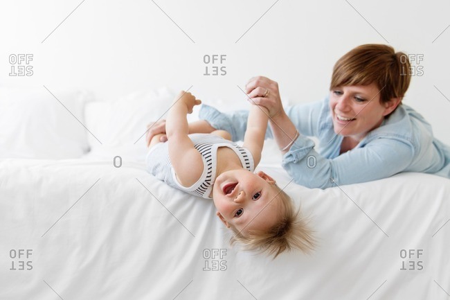 Mother holding baby upside down on white bed