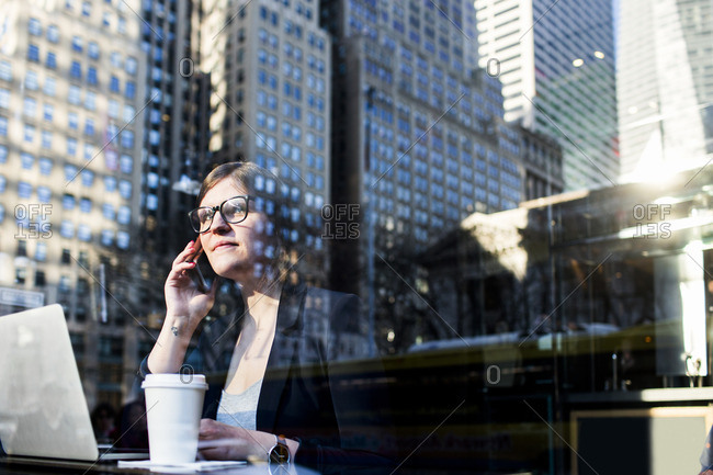 Businesswoman using phone seen through window with reflection of building