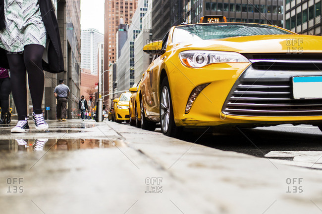 Low angle view of sidewalk by yellow taxis against buildings in city