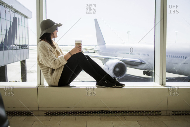Young woman holding disposable coffee cup and waiting at airport
