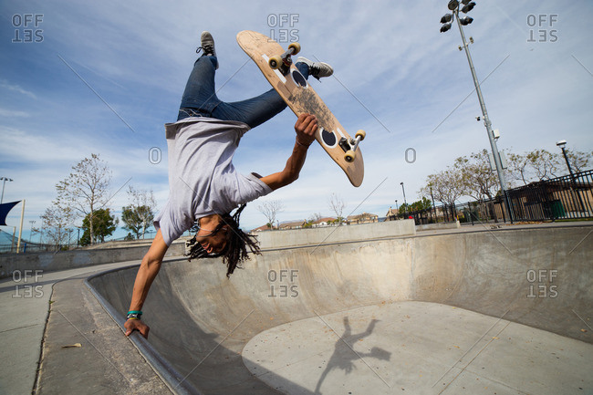 Young man doing skateboard trick upside down on edge of skateboard park