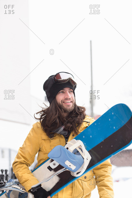 Smiling male snowboarder carrying snowboard in street