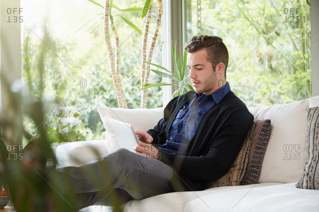 Man relaxing on sofa with feet up looking at digital tablet
