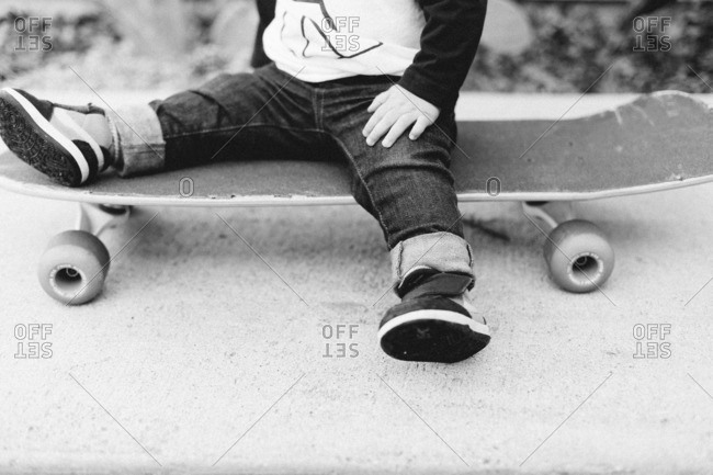 Legs of a toddler boy sitting on a skateboard