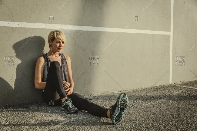 Portrait of a young woman in workout clothing sitting against a wall
