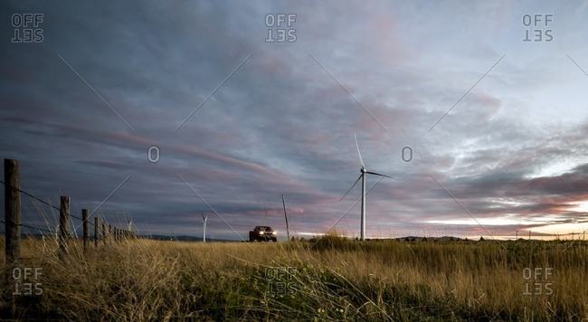 Car moving on grassy field by windmill against cloudy sky