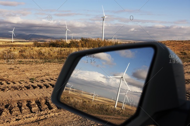 Windmills reflecting on side-view mirror of car at farm