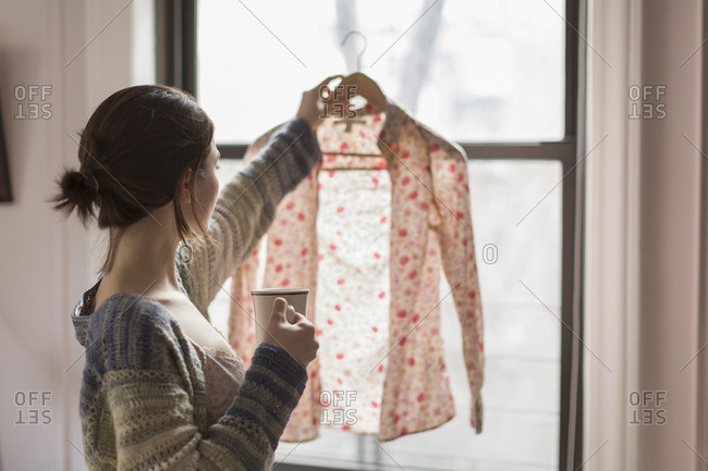 Young woman looking at a blouse and drinking coffee
