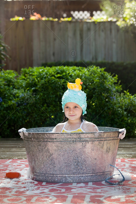 Portrait of girl in bubble bath in garden with rubber duck on head