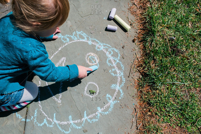Child sitting on pavement drawing with chalk