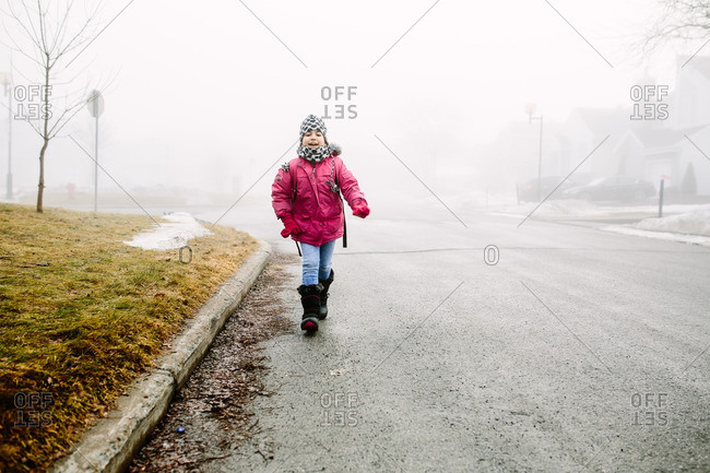 Girl walking down the street on a cold, foggy day in the winter