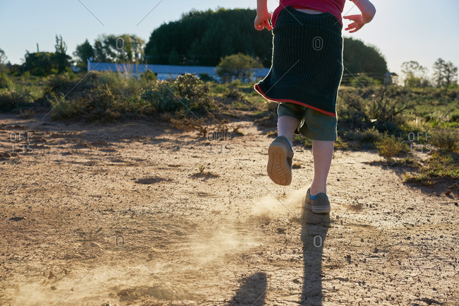 Boy kicking up dirt on a dirt patch in a scrubland