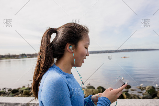 Young woman wearing headphones and holding mp3 player, English bay, Vancouver, Canada