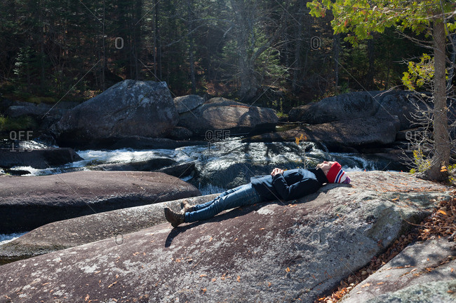 Male hiker lying on riverside rock, Rangeley, Maine, USA