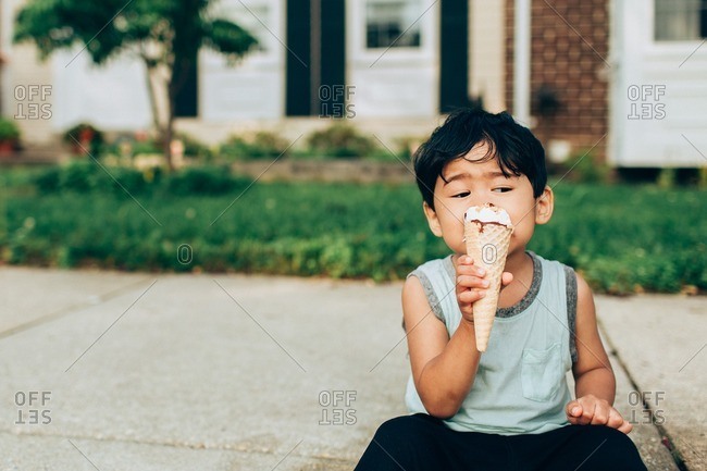 Asian boy sitting on sidewalk eating ice cream