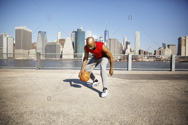 Full length of man playing with basketball on promenade against city skyline