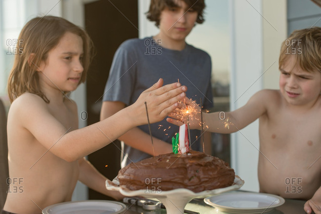 Boys blocking wind from sparklers on a birthday cake