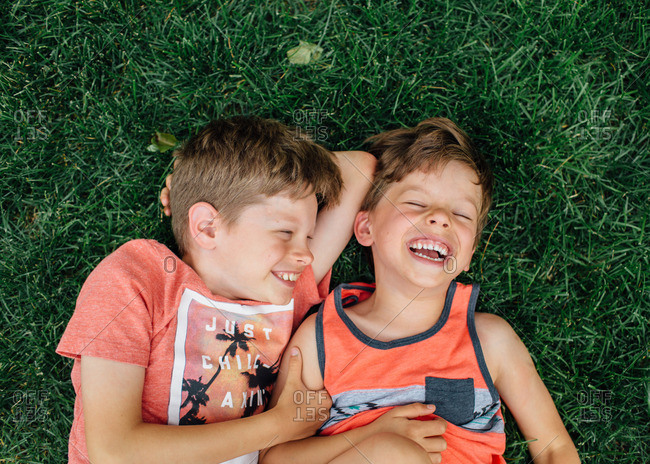 Young boys lay in grass laughing together.