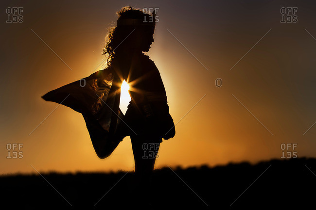Silhouette of young girl in winged fairy costume at sunset