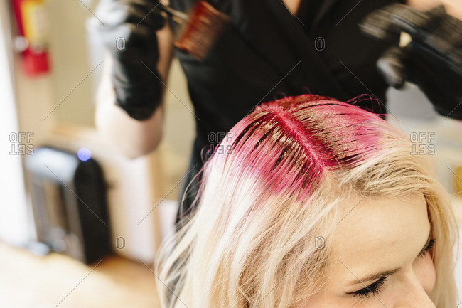 A stylist in gloves applying red hair dye to a client\'s blonde hair with a brush