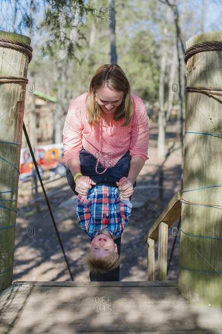Mother holding toddler son upside down on playground