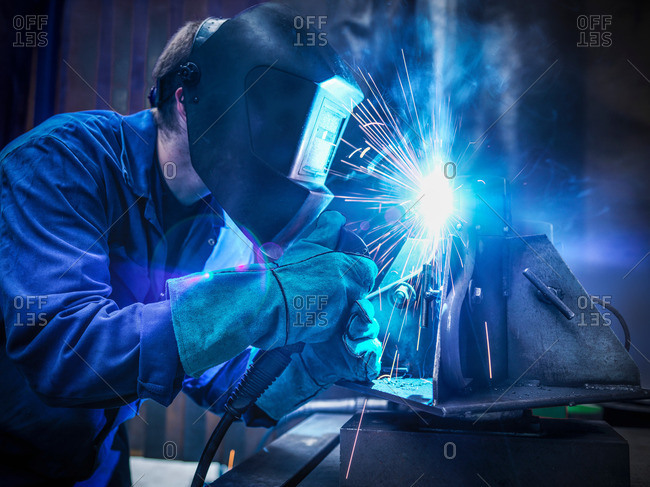 Welder wearing face mask and protective gloves in factory