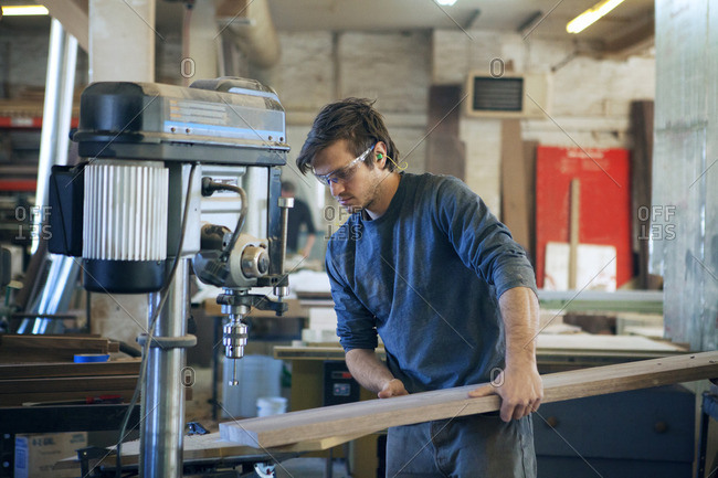 Male carpenter holding wooden planks under machinery at workshop