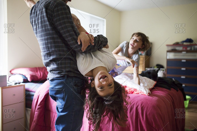 Portrait of cheerful girl being carried upside down by father in bedroom